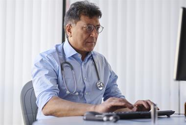 Male GP with stethoscope around neck typing on a computer
